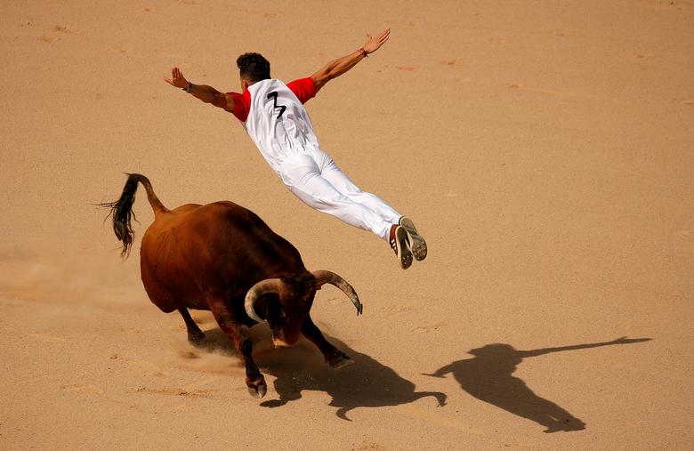 Тореадор перепрыгивает через быка на арене для боя во время фестиваля